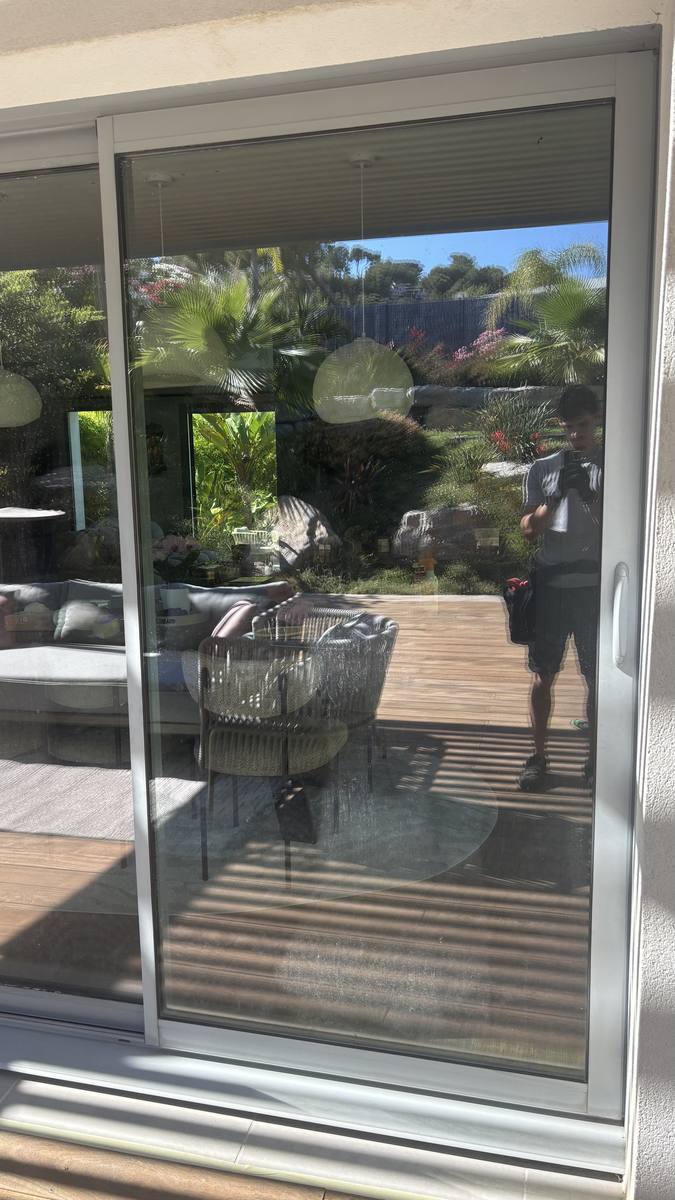 Technicien PluPropre nettoyant une baie vitrée donnant sur un jardin et une piscine